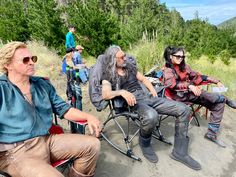 several people sitting in chairs on the side of a road with trees in the background