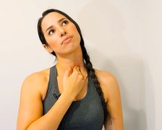 a woman standing in front of a white wall with her hands on her chest and looking up