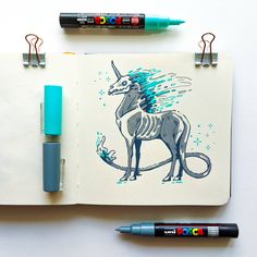 a notebook with a drawing of a unicorn on it and two markers next to it