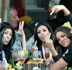 three women sitting at a table with wine glasses in front of them and one woman pointing to the side