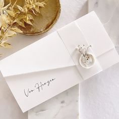 a white card with a ring on it next to some flowers and a gold plate