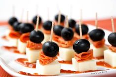 small appetizers with cheese and black olives are on a white platter