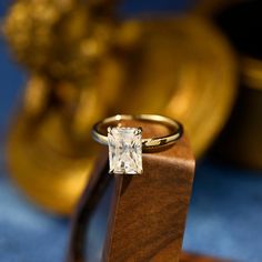 a diamond ring sitting on top of a wooden stand in front of a gold statue