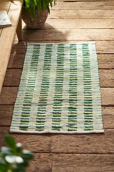 a green and white rug sitting on top of a wooden floor next to a potted plant