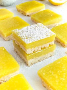 several pieces of yellow dessert sitting on top of a white tablecloth covered in powdered sugar