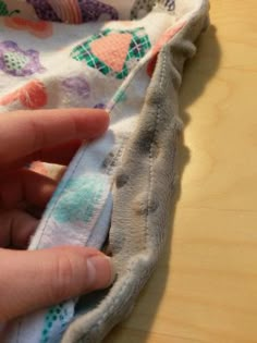 someone is sewing something on top of a cloth covered in flowers and leaves, with their fingers touching the fabric