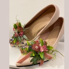 two pairs of shoes decorated with flowers and greenery on top of each other in front of a white background