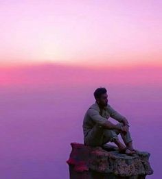 a man sitting on top of a rock next to the ocean at sunset or dawn