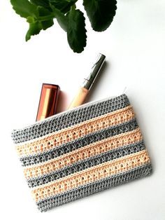 a crocheted purse next to a plant and lipstick on a white surface with green leaves