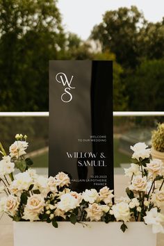 white flowers and greenery sit in front of a black sign that says welcome to the couple