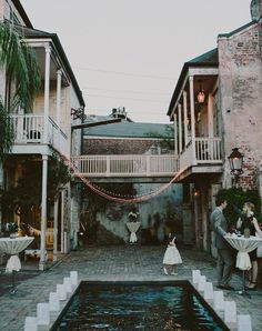 a bride and groom standing in front of an outdoor pool at their wedding reception with string lights strung across the walkway