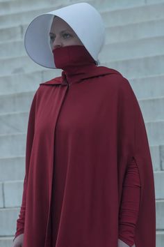 a woman wearing a red cape and white hat standing in front of steps with her hands on her hips