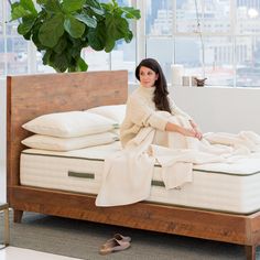 a woman sitting on top of a bed next to a plant in a room with large windows