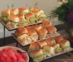 sandwiches and watermelon slices are on trays next to plates with flowers in the background