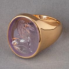 The griffin stands as a symbol of vigilant protection, woven deeply into historical and mythical narratives. Possessing the majestic body, tail, and hind legs of a lion combined with the awe-inspiring head, wings, and talons of an eagle, it represents an union of strength and vision. Materials: Amethyst intaglio set in a solid 18K gold signet ring Measurements: Approximately 16mm x 20mm Signet Ring Sketch, Intaglio Jewelry, Intaglio Ring, Head Wings, Signet Ring Men, Signet Rings, An Eagle, Dope Jewelry