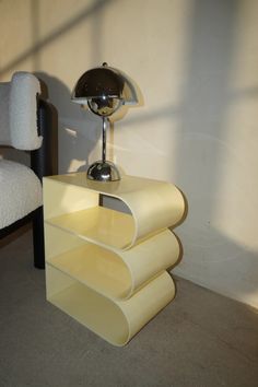 a lamp sitting on top of a yellow shelf next to a white chair and wall