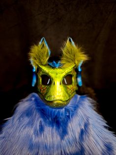 a yellow mask with blue feathers on it's head and eyes are shown in front of a black background