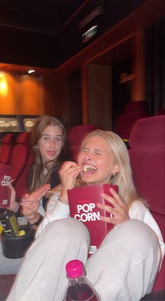 two women sitting in a movie theater eating popcorn