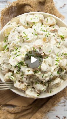 a white bowl filled with potato salad on top of a wooden table next to a fork