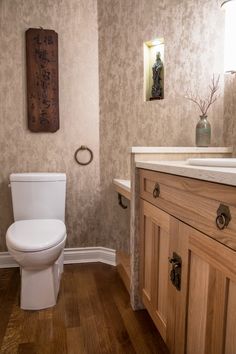 a white toilet sitting inside of a bathroom next to a wooden cabinet and counter top