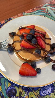 a plate topped with pancakes covered in chocolate syrup and strawberries next to a fork