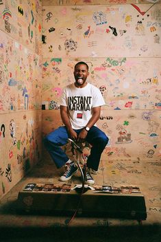 a man sitting on top of a wooden platform in front of a wall covered with stickers