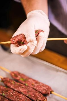 a person in white gloves holding chopsticks over meat on skewered sticks