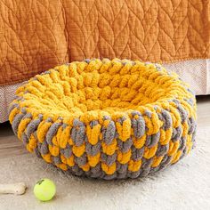 a yellow and gray knitted dog bed sitting on the floor next to a green ball