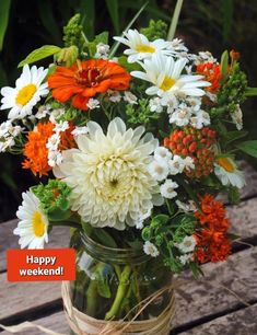 a mason jar filled with white, orange and yellow flowers on top of a wooden table