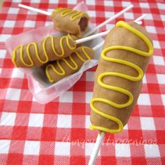 two hotdogs with yellow icing on a red and white checkered tablecloth