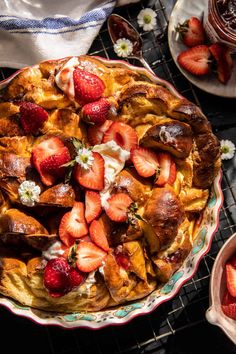 a pie with strawberries and cream on top sits on a cooling rack next to other desserts