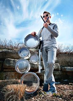 a man standing in front of a pile of pots and pans holding a cell phone up to his ear