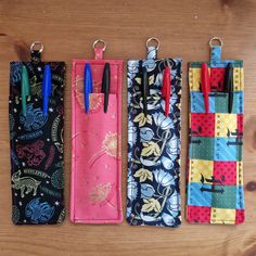 three pens and pencils are lined up in pouches on a wooden table top