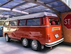 an orange vw bus parked next to a stop sign in a garage with other cars