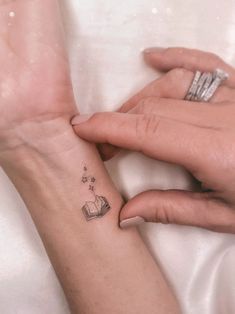 two hands holding each other with small tattoos on their wrist and the middle one has an open book