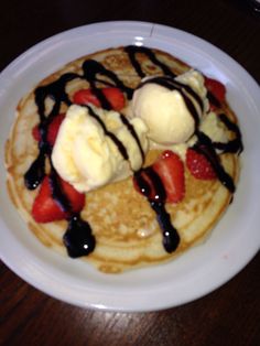 pancakes with ice cream, strawberries and syrup on a white plate sitting on a wooden table