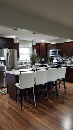 a large kitchen with wooden floors and stainless steel appliances in the center, surrounded by dark wood cabinetry