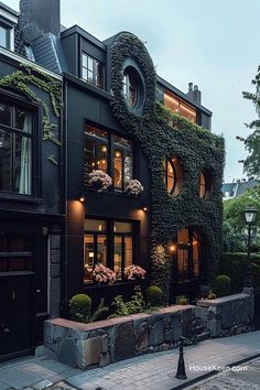 a black building with plants growing on it's side and windows that are lit up