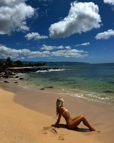 a woman laying on top of a sandy beach next to the ocean with clouds in the sky