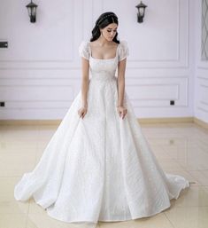 a woman in a white wedding dress standing on the floor with her hands behind her back