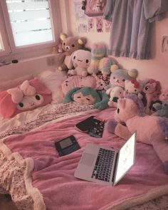 a laptop computer sitting on top of a bed covered in stuffed animals next to a window