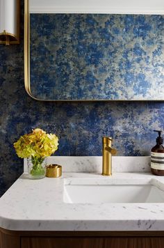 a bathroom sink with a mirror above it and flowers in the vase next to it