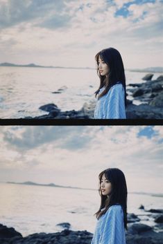 a woman standing on top of a rocky beach next to the ocean with clouds in the background