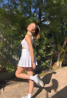 a woman in white tennis outfit posing for the camera with her tennis racket and shoes