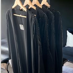 three black dresses hanging on wooden hangers in a room with a couch and chair