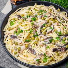 pasta with mushrooms and peas in a pan on a table next to some parsley