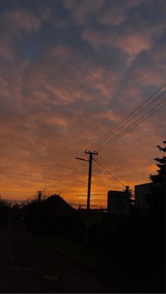 the sun is setting behind power lines and telephone poles in an urban area with houses on either side