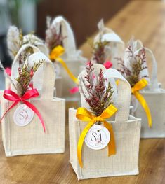 four small bags with flowers and ribbons tied to them on top of a wooden table