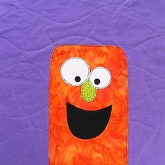 an orange and purple quilt with a face on it