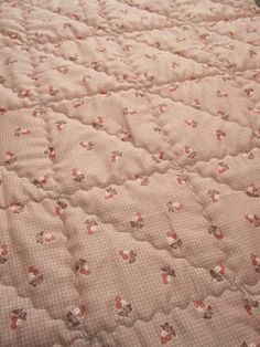 an unmade bed with pink and white bedspread that has flowers on it